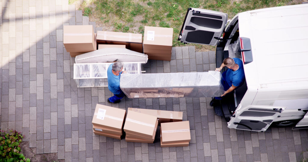Two men lifting furniture into a white moving van, surrounded by boxes