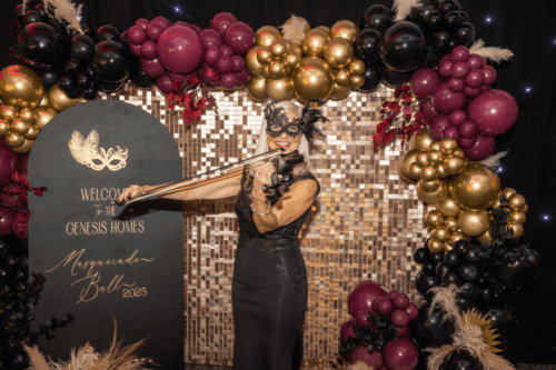 Woman in black dress playing the violin whilst wearing a masquerade mask