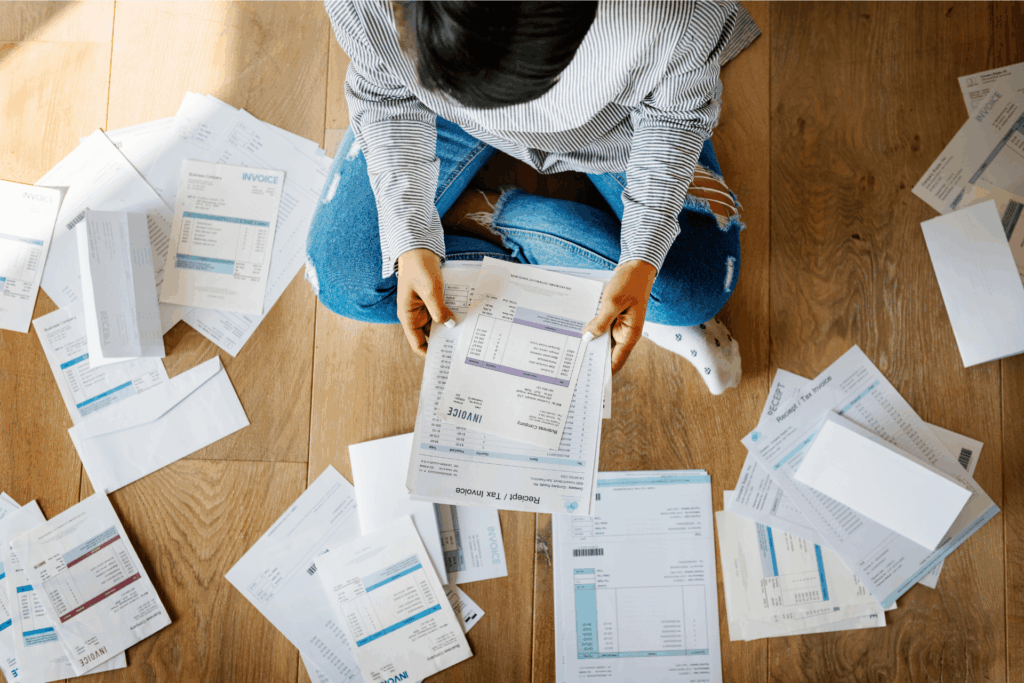 Woman sitting cross legged on the wooden floor surrounded by utility bills