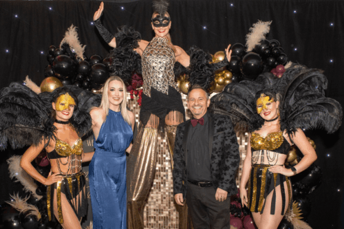 Women on stilts in the middle with event attendees either side and burlesque dancers