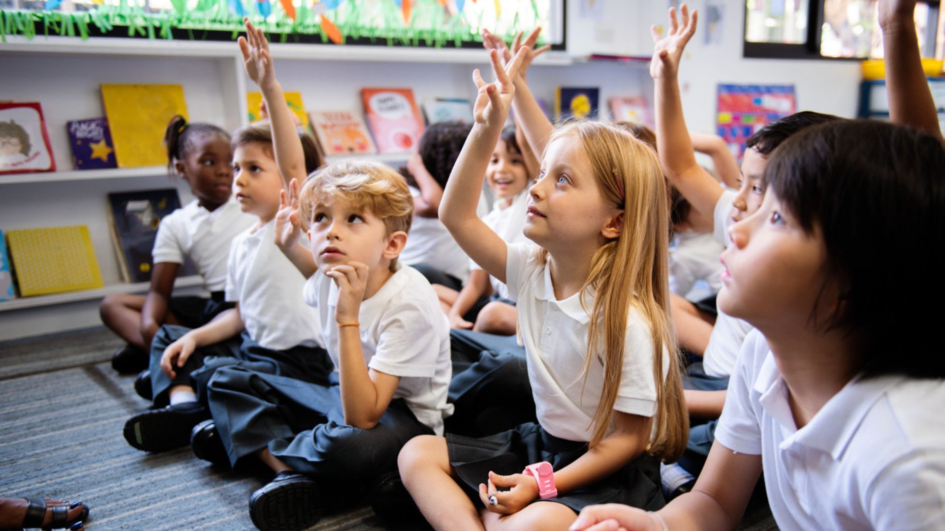 Primary school children sat on the floor with their hands up to answer a question