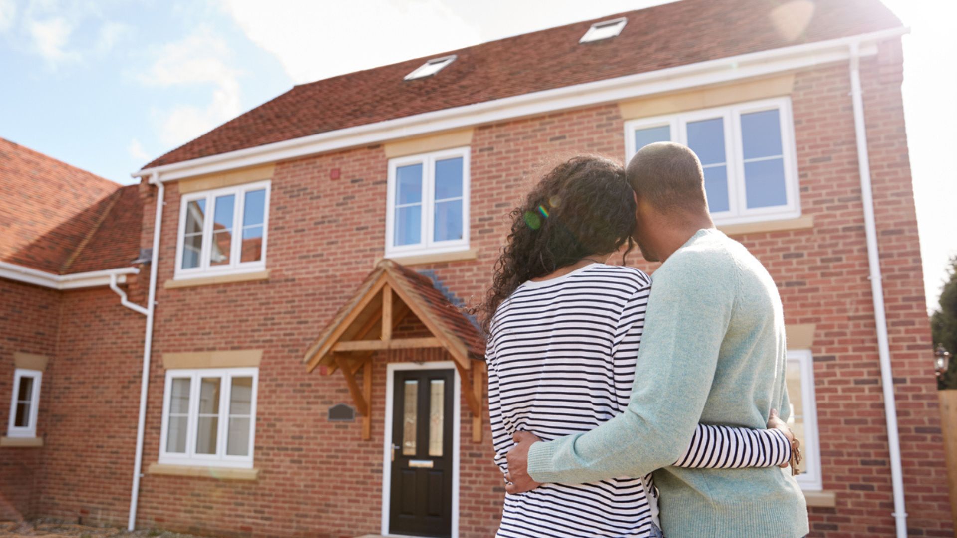 young couple standing outside the front of their new build home 